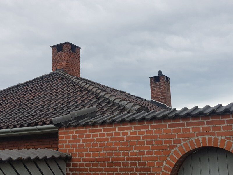 Valmtag med to skorstene i tegltagsten, set nedefra mod gråt himmel.