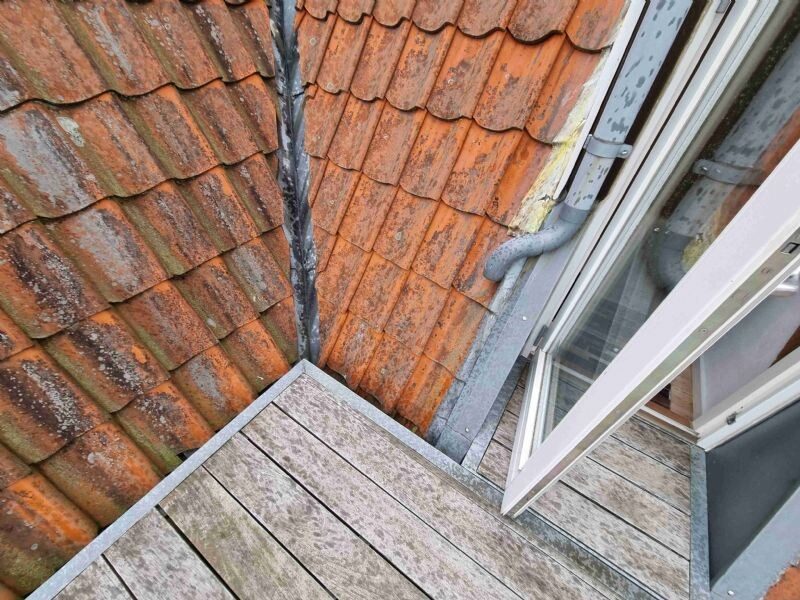 Nærbillede af skotrende i zink mellem tegltag og kvist med ovenlysvindue, set fra tagfladen.