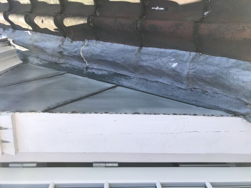 Nærbillede af en blyinddækning ved en kip eller grat med synlige revner og gammel udbedring med tape.