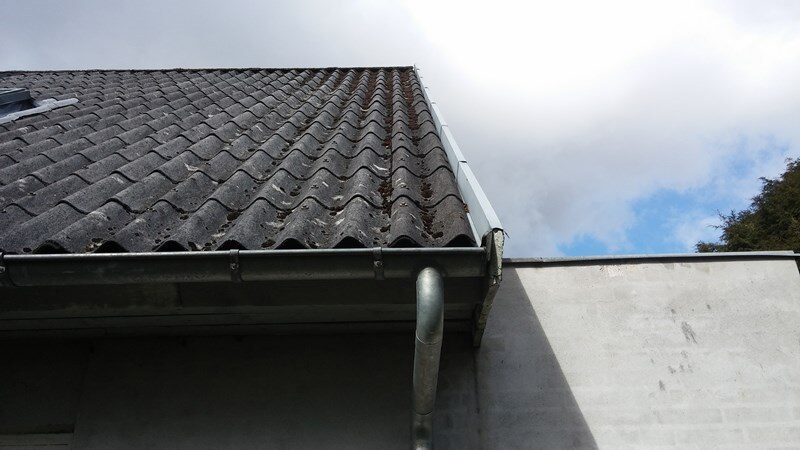 Nærbillede af tagfod med bølgeeternit, tagrende og nedløbsrør, set skråt nedefra ved gavl.