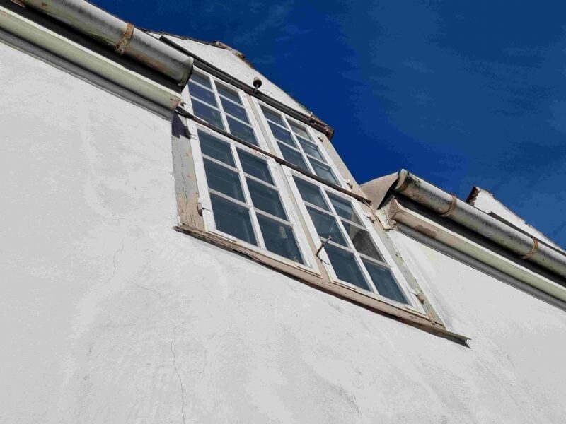 Nærbillede nedefra af en kvistgavl med gamle sprossevinduer og zinktagrender på en hvidpudset gavl.