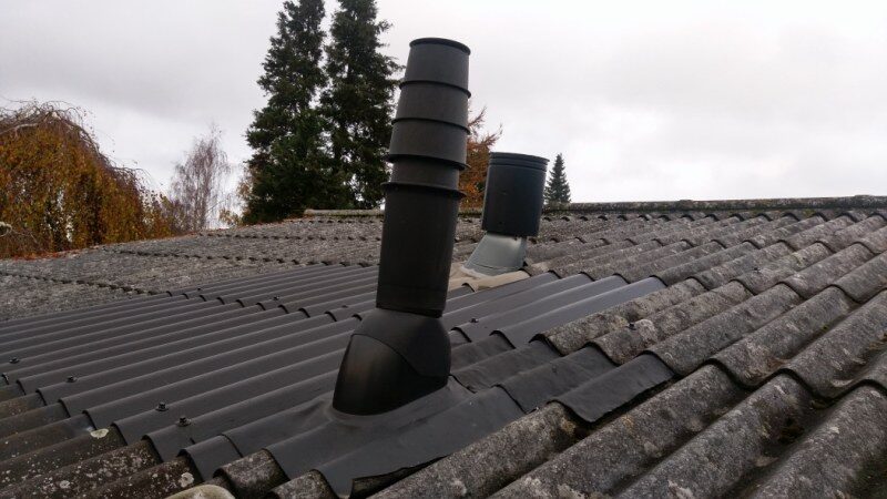 To sorte ventilationshætter monteret på tagflade med betontagsten, den ene med grå gummimanchet ved inddækningen.