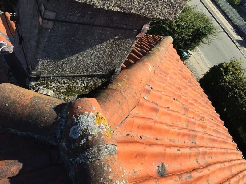 Nærbillede af rygningssten på teglstenstag med gule og grå lavbelægninger, fotograferet fra oven ned mod gaden.