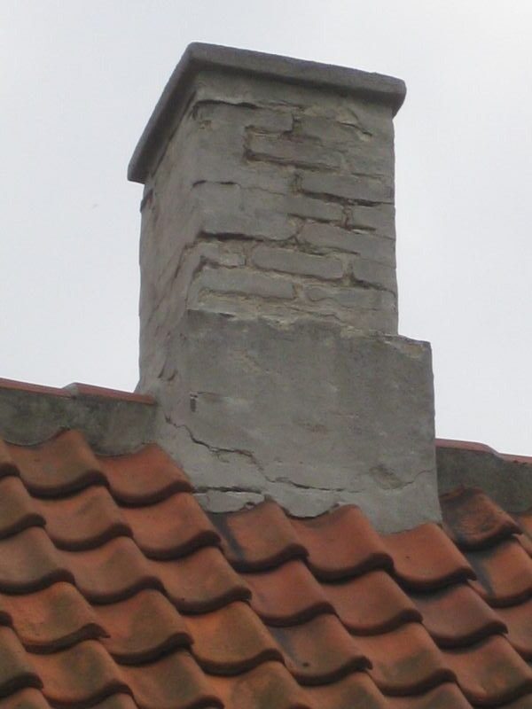 Nærbillede af en skorstenspibe med grov betoninddækning og revnet murværk, fotograferet nedefra mod himlen.