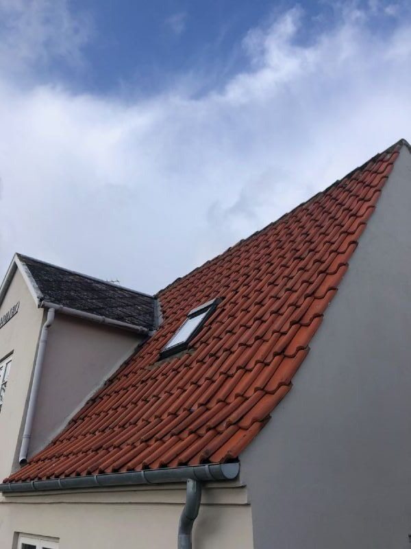 Nærbillede nedefra af tagryg med røde vingetagsten, lille ovenlysvindue og tagrende ved gavl.