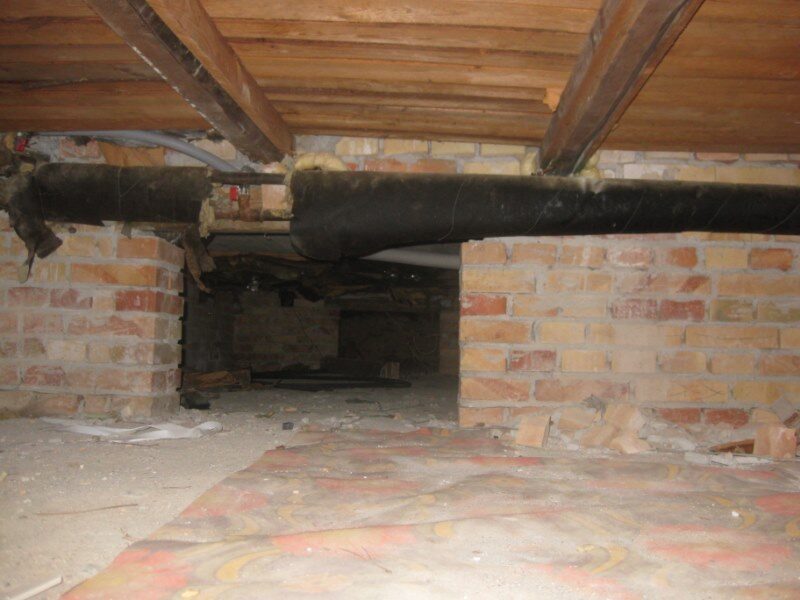 Krybekælder eller uudnyttet loft/kælderrum med murede skillevægge, bjælkelag og en tyk isoleret rørføring.