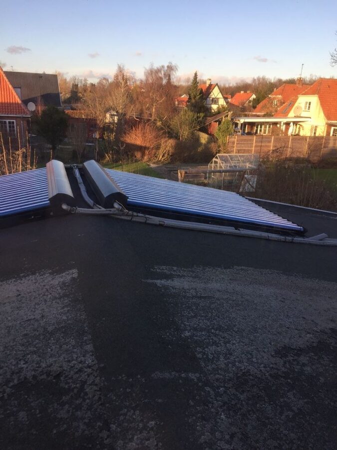 Solfangere med vakuumrør monteret på fladt tagpaptag med udsigt til nabohuse i baggrunden.